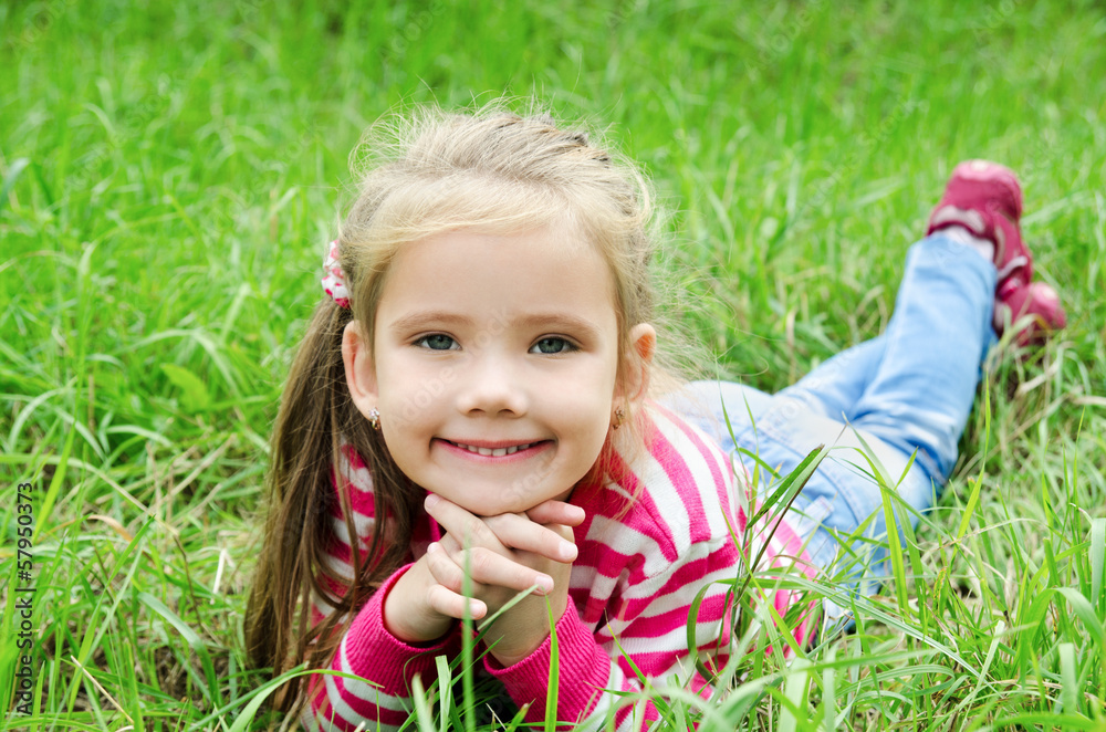 Cute smiling little girl lying in grass on the meadow Cute smiling little girl lying in grass on the meadow
