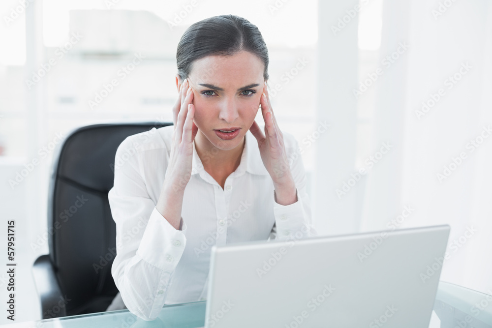 Businesswoman suffering from headache in front of laptop Businesswoman suffering from headache in front of laptop