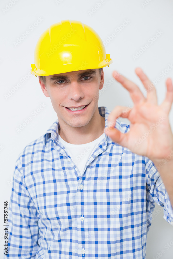 Smiling handyman in yellow hard hat gesturing okay sign