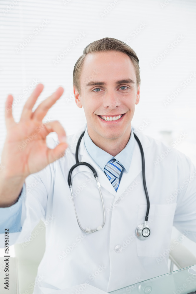 Smiling doctor gesturing okay sign at medical office Smiling doctor gesturing okay sign at medical office