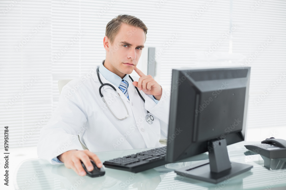 Serious doctor using computer at medical office Serious doctor using computer at medical office