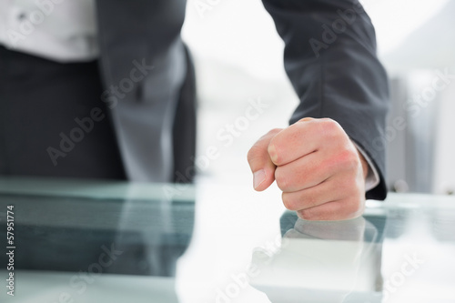 Mid section of businessman with clenched fist on office desk