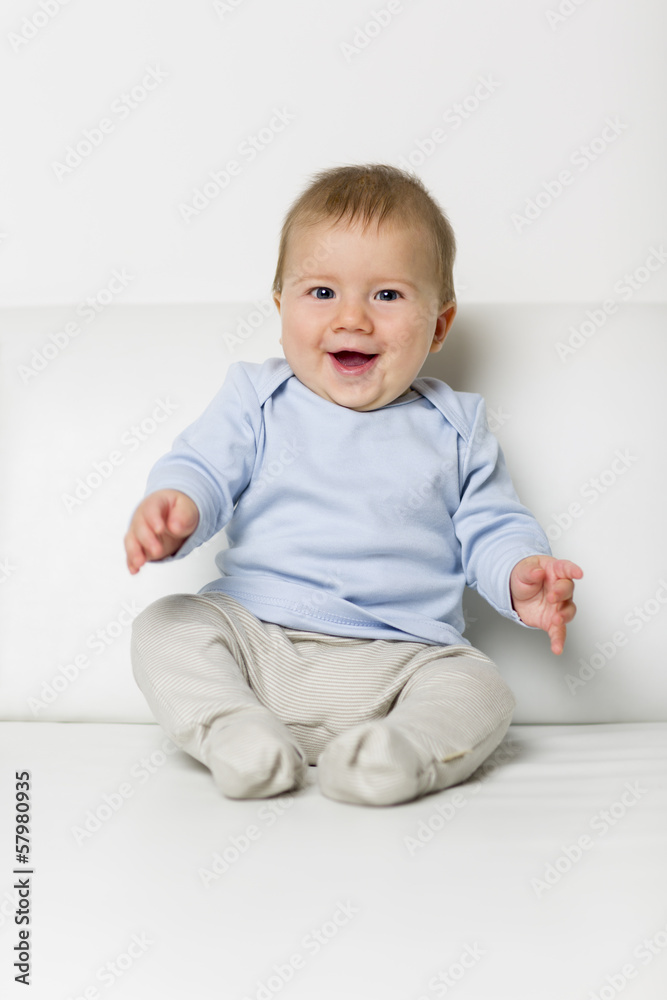Portrait of sweet overjoyed baby boy sitting on sofa.