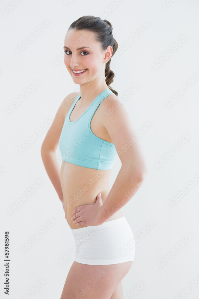 Toned young woman with hands on hips against wall Toned young woman with hands on hips against wall