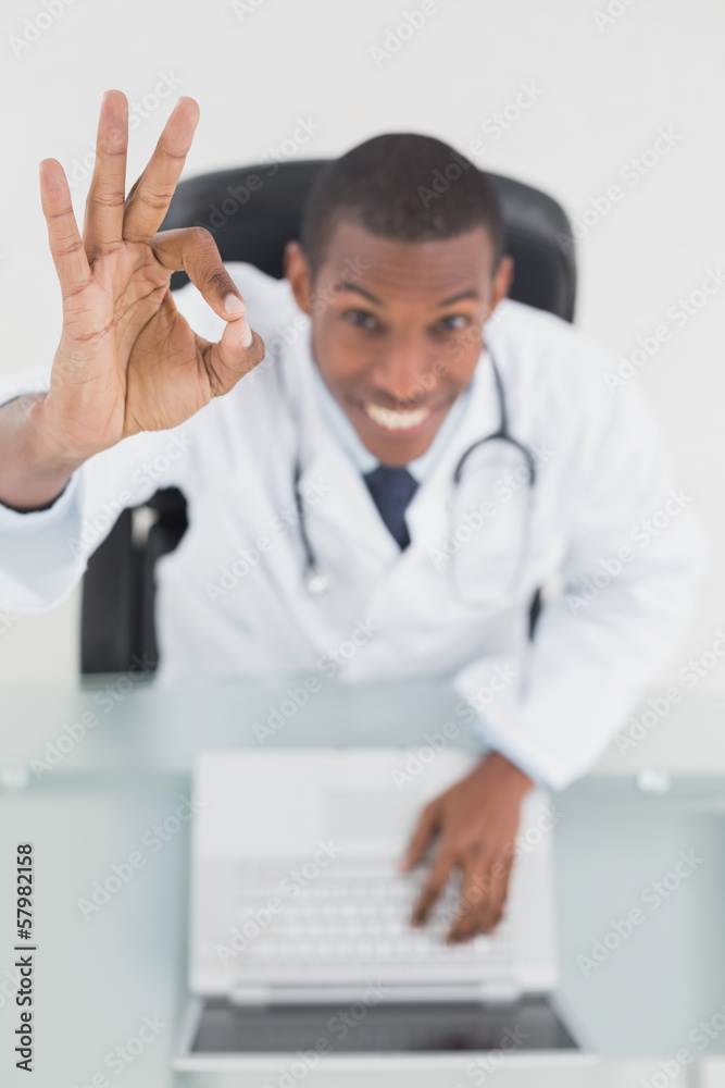 Overhead of a smiling doctor with laptop gesturing okay sign Overhead of a smiling doctor with laptop gesturing okay sign
