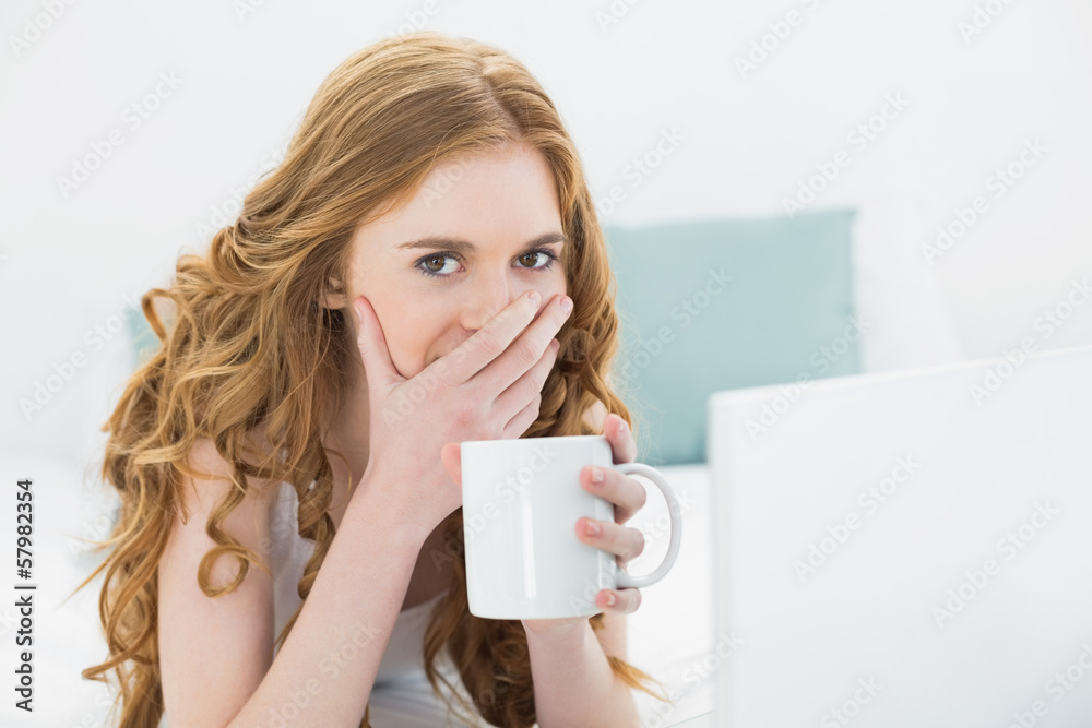 Shocked blond drinking coffee while using laptop in bed Shocked blond drinking coffee while using laptop in bed