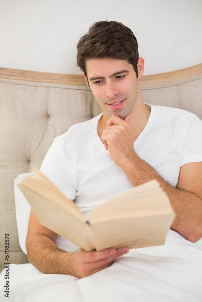 Relaxed young man reading book in bed Relaxed young man reading book in bed