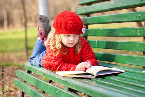 Little girl reading book on a bench