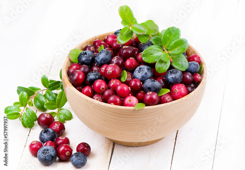 Blueberry and cowberry with green leaflets in wooden cup