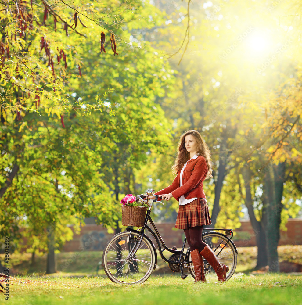 Fototapeta premium Young female with bicycle relaxing in a park on a sunny day