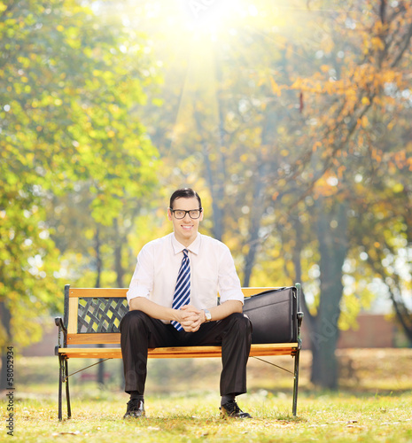 Relaxed businessman sitting on bench in a park on sunny day