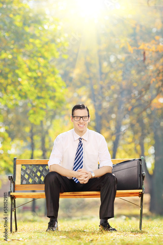 Smiling young businessman sitting on a wooden bench in park