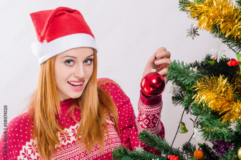 Woman with Santa hat decorating the Christmas tree with red ball Woman with Santa hat decorating the Christmas tree with red ball