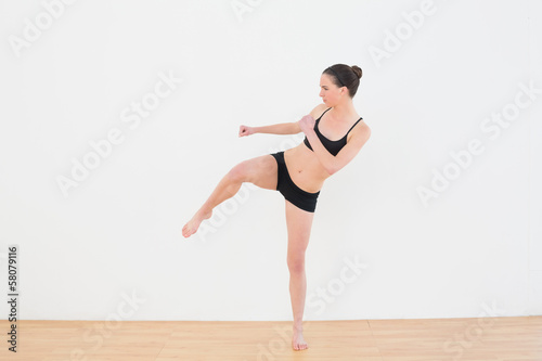 Sporty fit woman performing an air kick in fitness studio