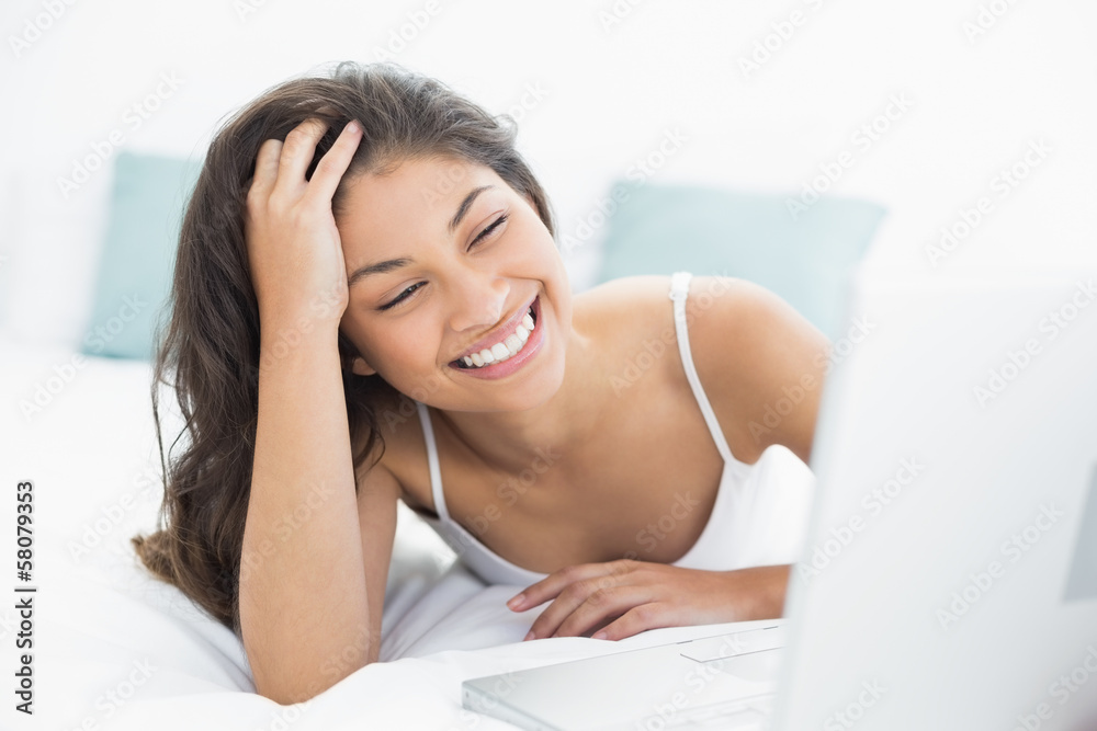 Cheerful casual woman using laptop in bed
