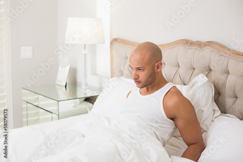 Thoughtful young bald man sitting in bed