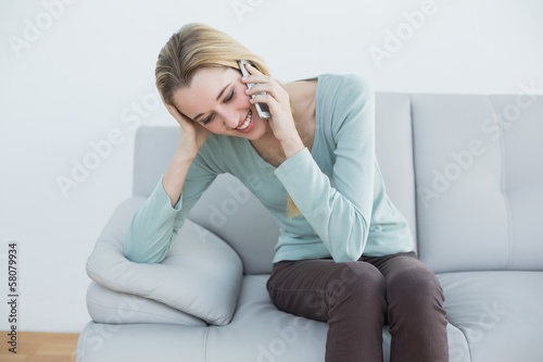 Cute blonde woman phoning happily sitting on couch