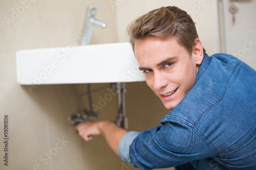 Smiling plumber repairing washbasin drain
