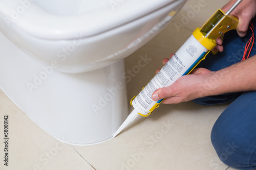 Plumber fixing toilet in a washroom with silicone cartridge