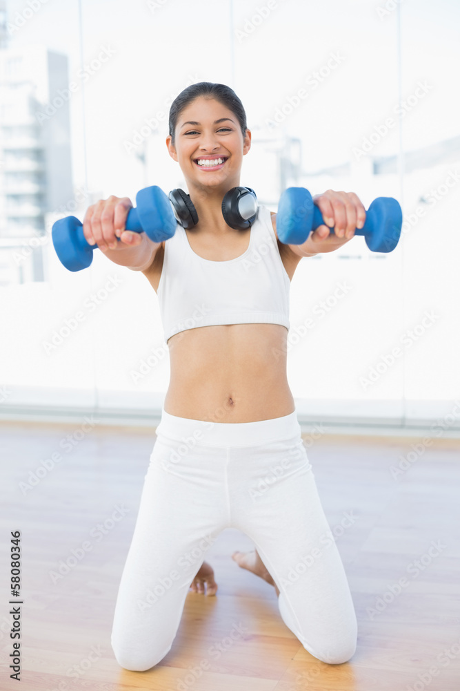 Cheerful woman exercising with dumbbells in fitness studio