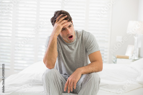 Sleepy young man sitting and yawning in bed © lightwavemedia