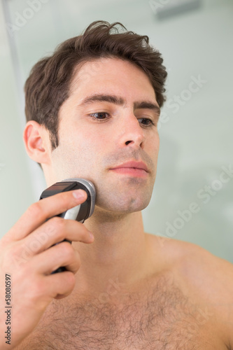 Handsome shirtless man shaving with electric razor