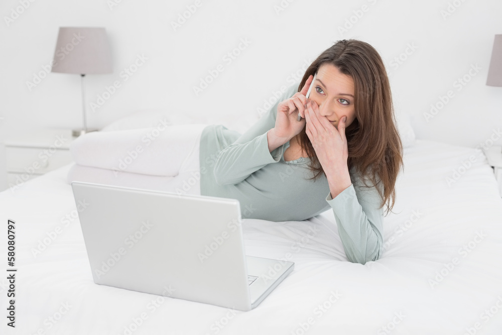 Shocked casual woman using cellphone and laptop in bed Shocked casual woman using cellphone and laptop in bed