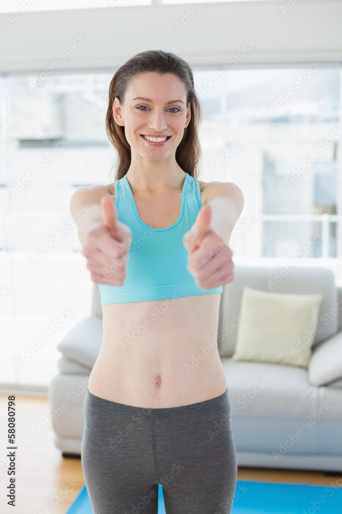 Toned woman gesturing thumbs up in fitness studio