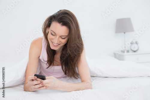 Happy woman looking at mobile phone in bed