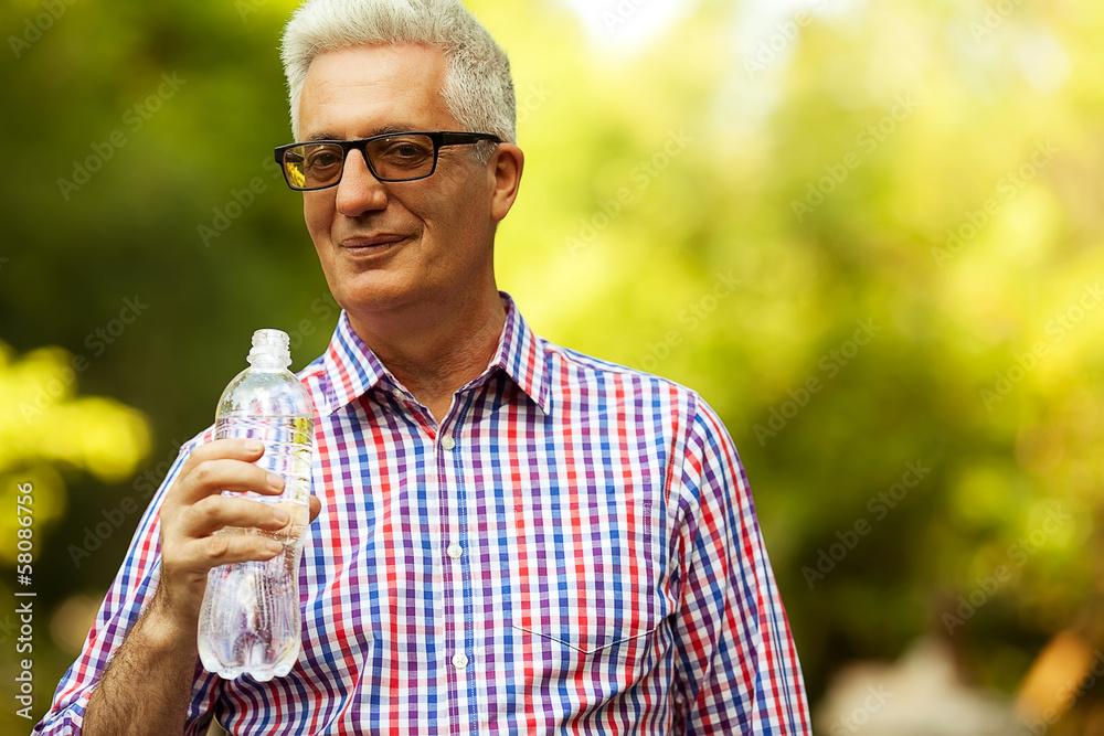 Fototapeta premium Smiling happy mature (old) man holding bottle of water