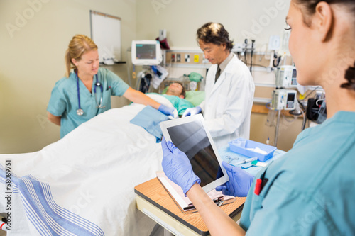 Nurse Holding Digital Tablet While Colleague And Doctor Operatin