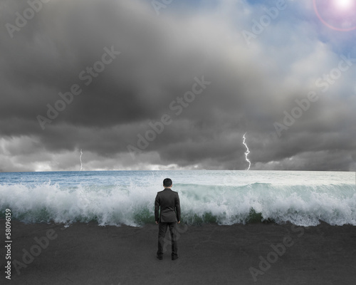 Businessman standing toward waves and cludy sky with Lightning ,