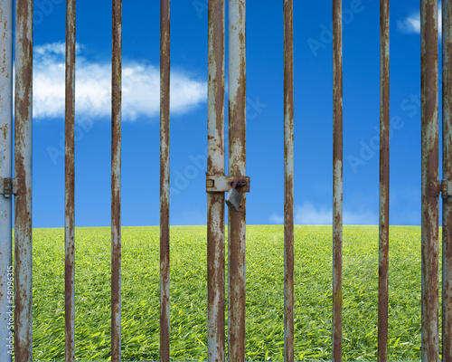 Locked rusty door with beautiful landscape, green meadow blue sk