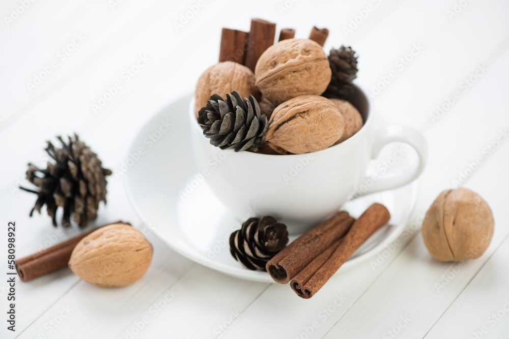 Walnuts, cinnamon and fir-cones, white wooden background