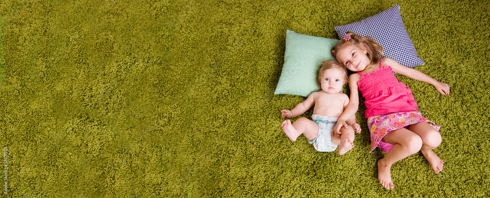 Two happy sisters lie on carpet
