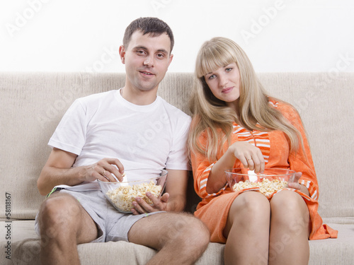 Молодая пара сидит на диване и ест попкорн