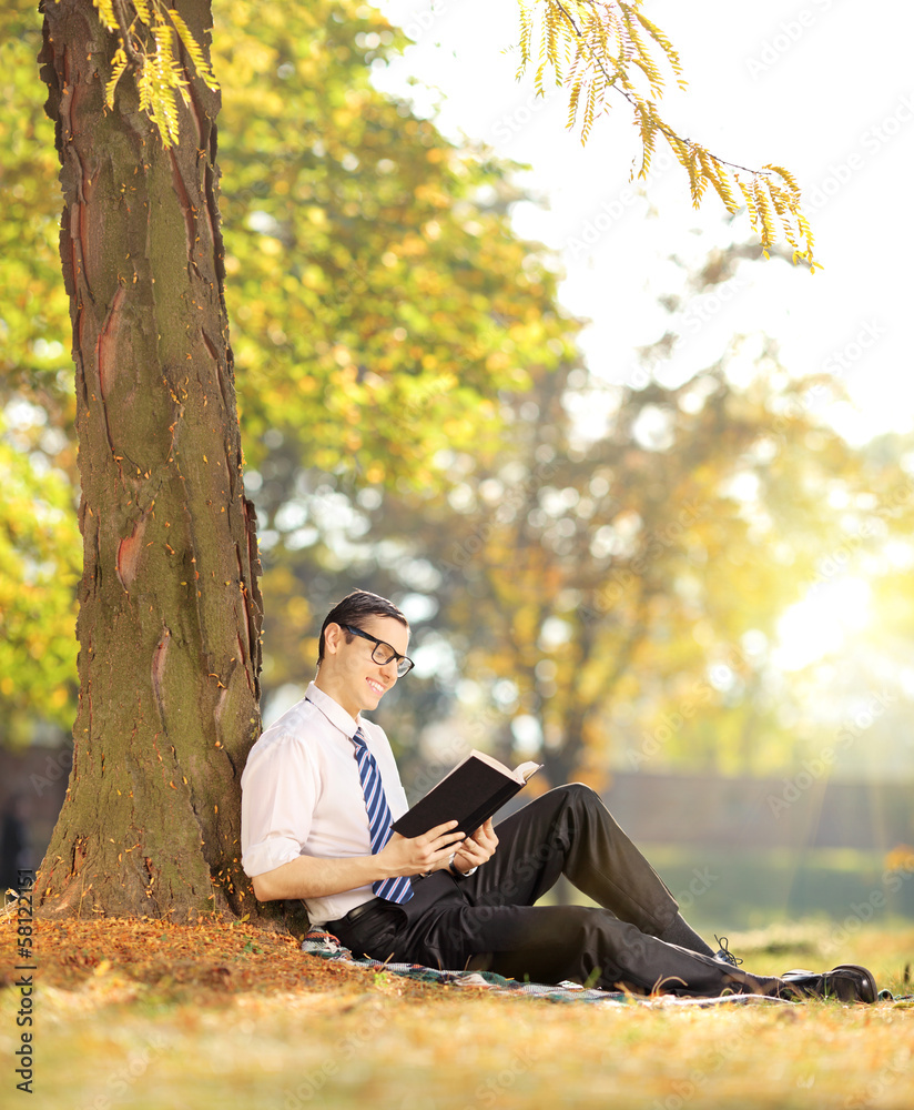 Young male sitting on a grass and reading a book in park
