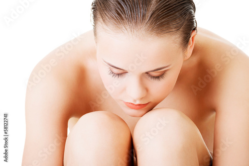 Attractive nude woman sitting holding herself. Closeup.