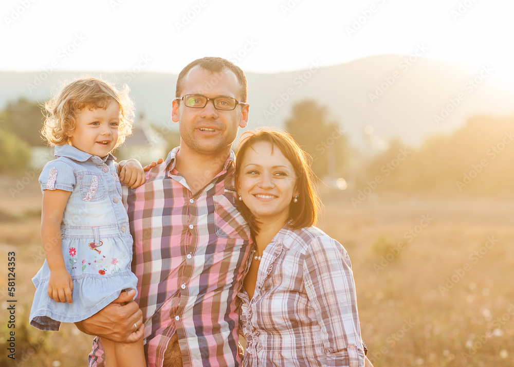 Fototapeta premium Happy mother, father and daughter in the mountains at sunset