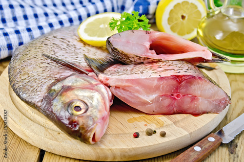 Bream raw on a round board with a knife and oil