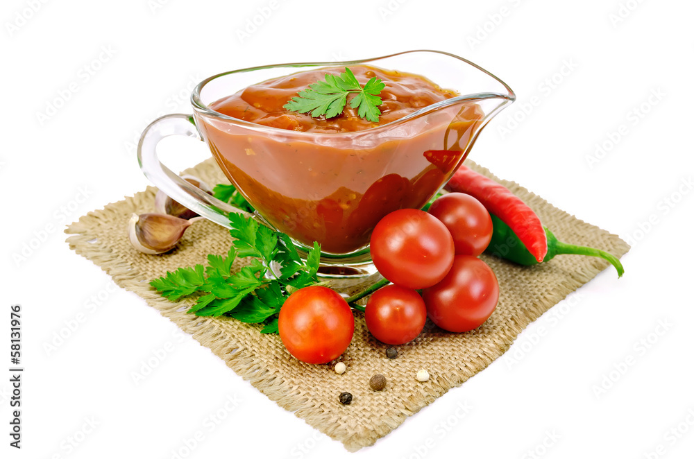 Ketchup in a glass gravy boat with vegetables on sacking Ketchup in a glass gravy boat with vegetables on sacking
