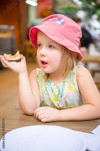 Adorable girl in pink hat eat pizza in street pizzeria
