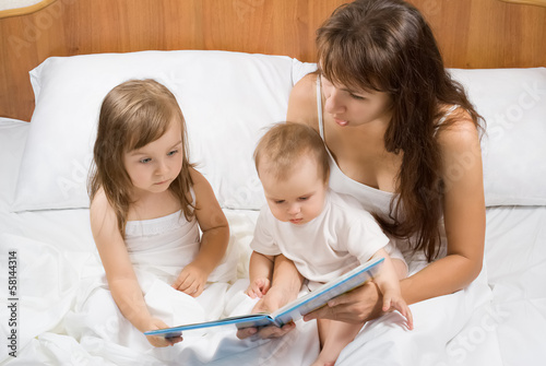 Mother reading bed time story book to children in bed