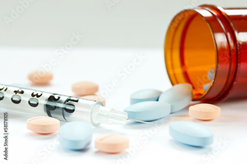 Pills spilling out of pill bottle and Syringe isolated on white