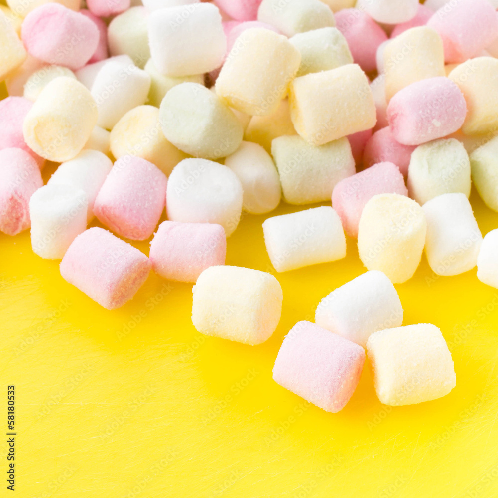 A pile of small colored puffy marshmallows on bright yellow ba A pile of small colored puffy marshmallows on bright yellow ba