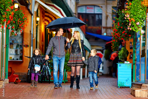 happy family walking under the rain on cozy colorful street © Olesia Bilkei