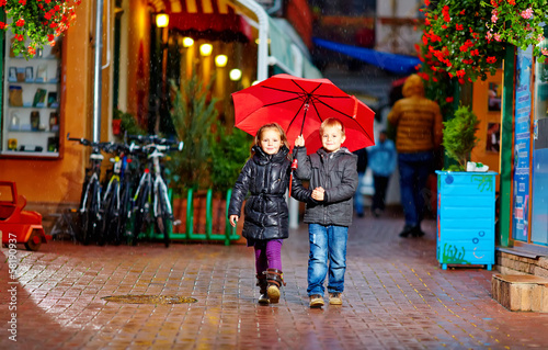 cute children walking colorful evening street, under the rain © Olesia Bilkei