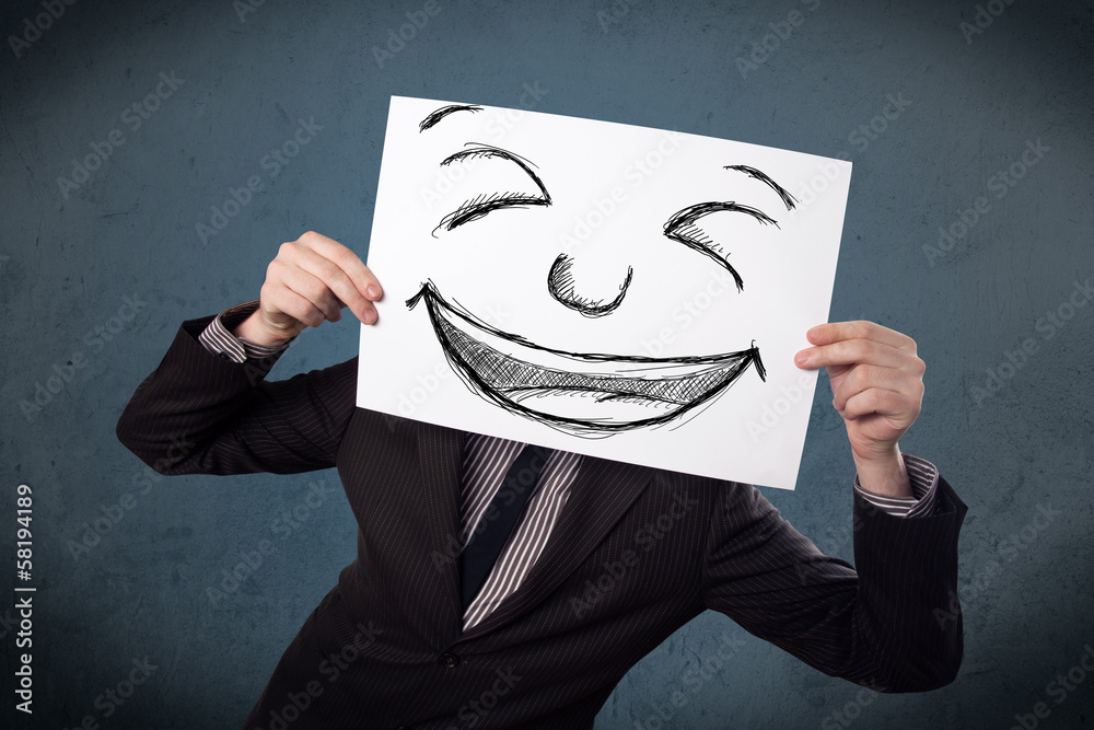 Businessman holding a paper with smiley face in front of his hea Businessman holding a paper with smiley face in front of his hea