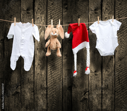 .Baby clothes and santa hat on a clothesline, wooden background photo