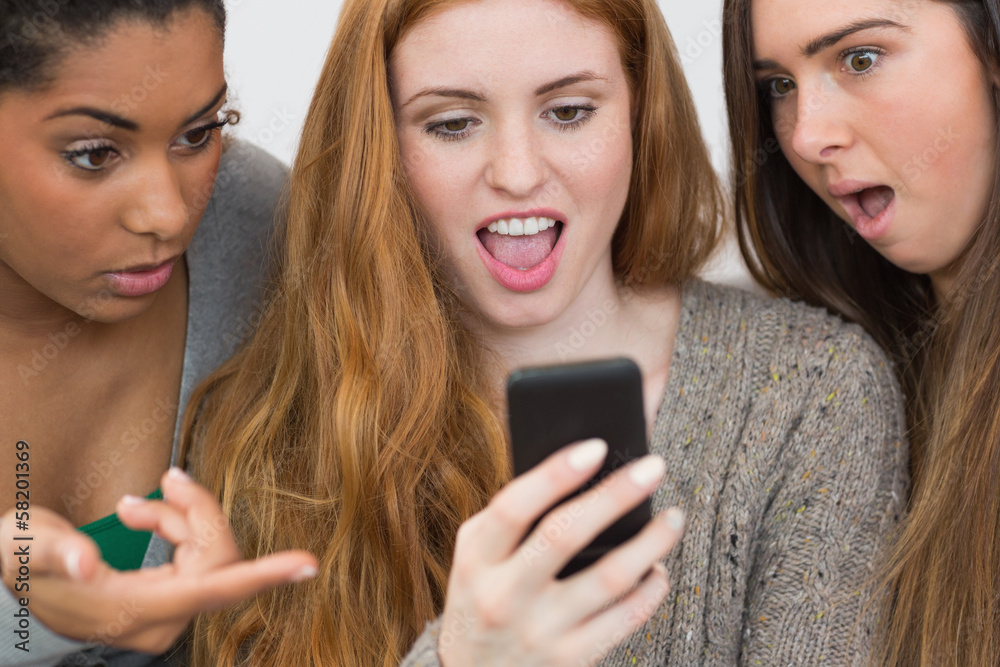 Shocked female friends looking at mobile phone together Shocked female friends looking at mobile phone together